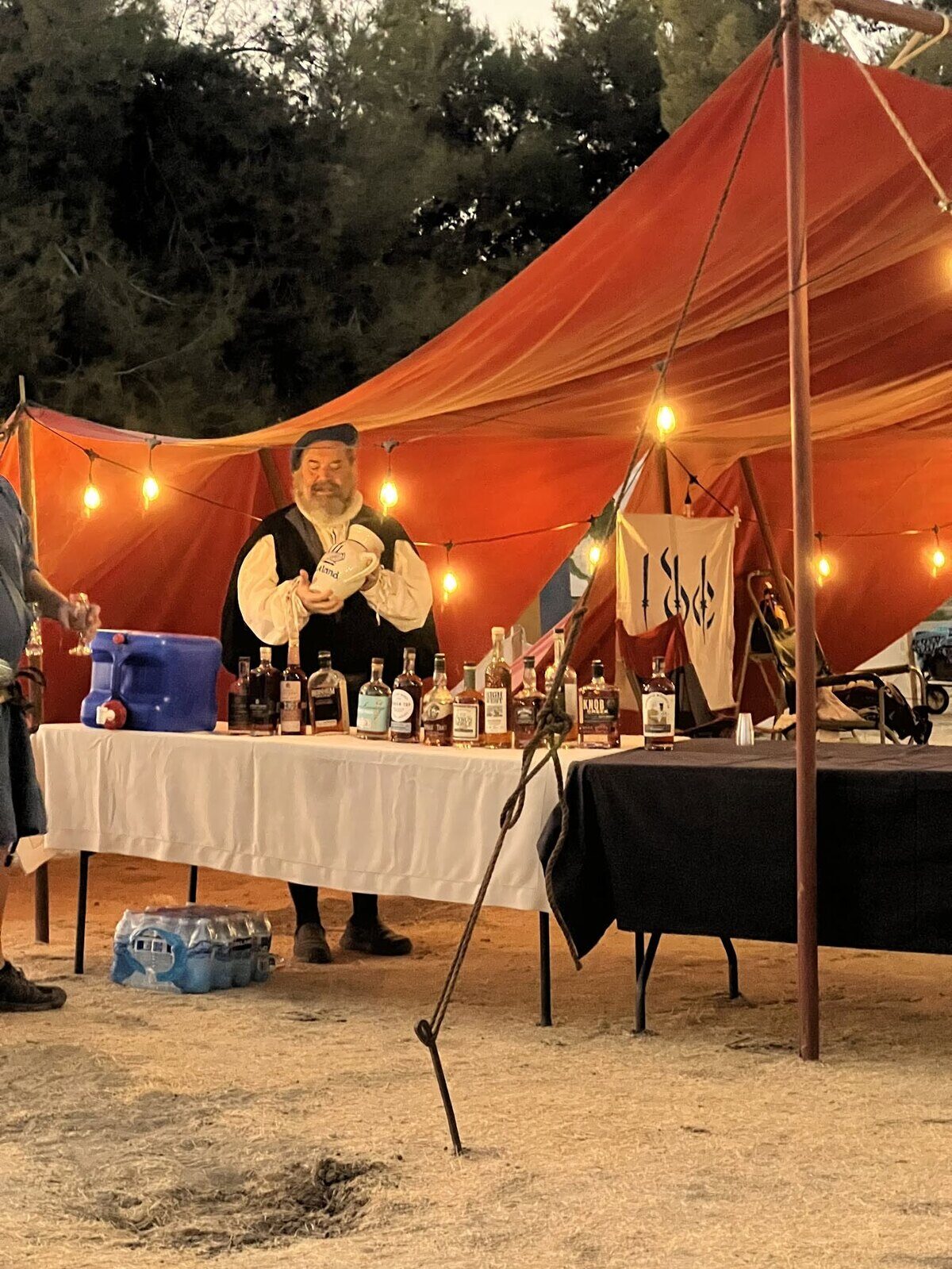 The 3DC camp at dusk: a red canopy hung with lights, a table of bottles and the 3DC banner